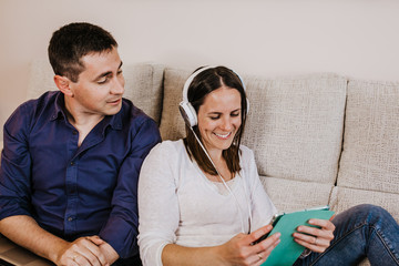 .A young couple sitting on the couch at home surfing the internet with their tablet and laptop, looking for information for their next holidays. Having fun together, relaxed and carefree. Lifestyle