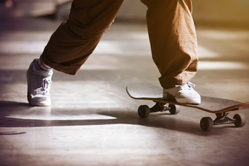 A guy in beige loose pants and white running shoes pushes off the floor and rides a skateboard, illuminated by the lighting of different colors.