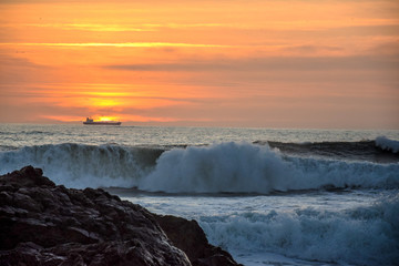 Obraz premium sunset over the sea with wave in front and ship in the background
