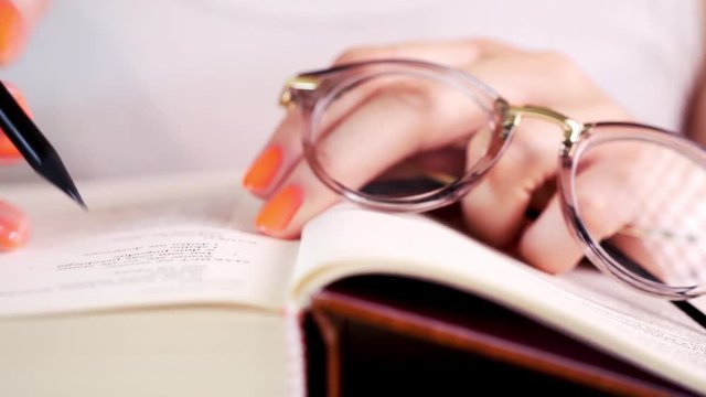 view of a woman's hand reading an old book and writing notes