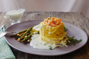 Delicious fettuccine nest with shrimp filling with white sauce next to grilled asparagus stems and poached egg ready to eat