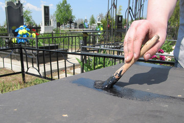 A man uses a brush to paint an iron table with black color