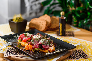 Veal tartare on pumpkin puree with parmesan, lettuce and tomatoes, on a black plate on the table in the restaurant. close-up. top view 
