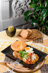 Delicious breakfast with boiled eggs, pumpkin puree, lettuce, cheese and fresh bread on a black plate on a yellow set on a wooden table in a restaurant. Close up. Space