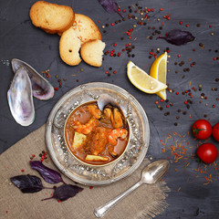 French seafood soup. Bouillabaisse ear of seafood. Vintage silver plated plate and spoon. Black background, top view. Free space for inscriptions. Still life concept.