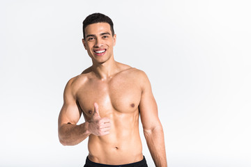 handsome sportive mixed race man smiling and showing thumb up on white