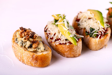 Brushetta set for an aperitif. Variety of small sandwiches with tomatoes, parmesan cheese, avocado and walnut served on a white background
