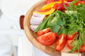 Organic farm. Fresh vegetables in wooden plate: yellow and red bell pepper, onion, tomato and cucumbers.