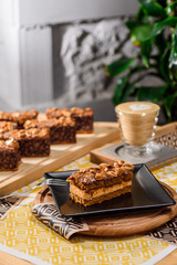 Chocolate brownie with nuts on a black plate on a yellow set on a wooden table in a restaurant. Cappuccino on the background. Close up. Space