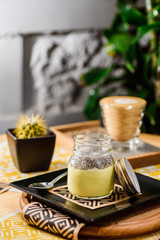 Coffee and yellow chia pudding in a jar on a wooden table in the restaurant. Beautiful chia pudding serving in a restaurant on a yellow background. close up