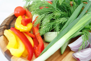 Organic farm. Fresh vegetables in wooden plate: yellow and red bell pepper, onion, tomato and cucumbers.