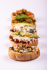 Brushetta set for an aperitif. Variety of small sandwiches with tomatoes, parmesan cheese, avocado and walnut served on a white background
