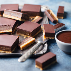 Chocolate caramel slices, bars, millionaires shortbread on a metal tray. Blue background. Close up.