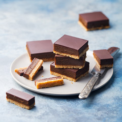 Chocolate caramel slices, bars, millionaires shortbread on a grey plate. Blue background.
