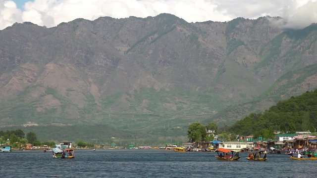 Wide shot of distant mountains towering above several shikara boats in Dal lake