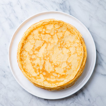 Crepes, thin pancakes on a white plate. Marble background. Copy cpace. Top view.