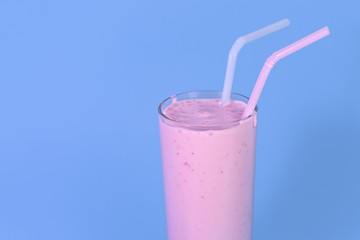 glass of pink strawberry milkshake or cocktail with berry on blue background