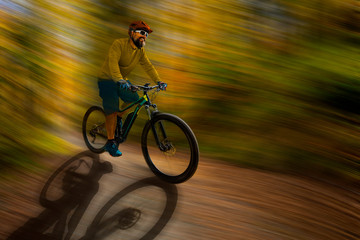 Naklejka na ściany i meble Mountain biker riding on bike in spring mountains forest landscape. Man cycling MTB enduro flow trail track. Outdoor sport activity. Motion Blur picture.