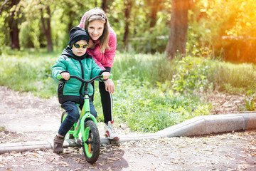 Young girl teaches her younger brother to ride a bike at sunset. They stopped for a rest and smiled happily