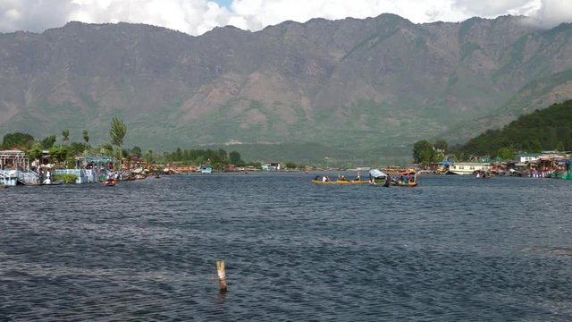 Wide panning shot of Dal lake stretching into the distance, with tall mountains behind it