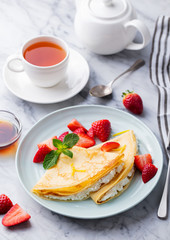 Crepes, thin pancakes with fresh strawberry and ricotta with cup of tea. Marble background.