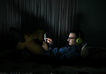 Man watching tv series in a tablet sitting on a bed in the night at home