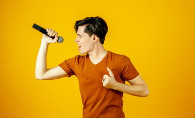 Fototapeta na wymiar Karaoke man singing a song into a microphone, on a yellow background. A funny man holds a microphone in his hand at the karaoke singer singing a song! Pivets on a yellow background