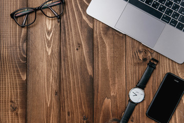 Laptop, smart phone, glasses and watch on wooden table.