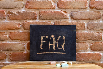 Black board with the word FAQ drown by hand on wooden table on brick wall background.
