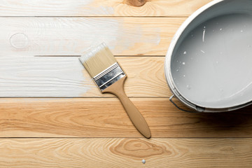 top view of brush and bucket of white paint on wooden surface