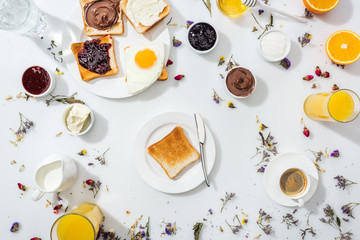 top view of plates with tasty toasts and knife near drinks and oranges on white