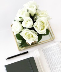 Baselland, Switzerland - 03.05.2019. Bible flat lay on a white Table with different accessories; white roses, grey journal, black pen, golden vase, etc. 