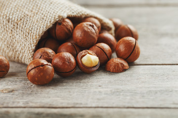 Macadamia nuts spilled out of the bag on a wooden background close-up with one peeled nut