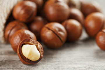 Macadamia nuts spilled out of the bag on a wooden background close-up with one peeled nut