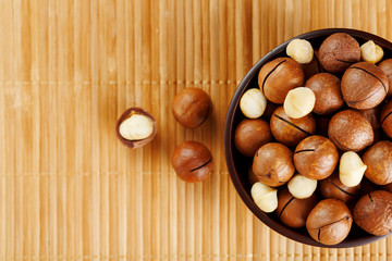 Macadamia nut on bamboo texture in a wooden cup, peeled and not peeled walnut, top view