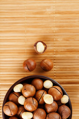 Macadamia nut on bamboo texture in a wooden cup, peeled and not peeled walnut, top view