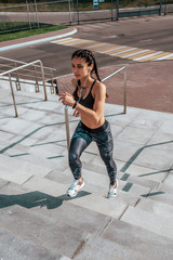 Girl runs in the summer in the city, on morning run. Background steps. Clothing leggings top. Phone earphones. Fitness concept jogging, lifestyle.