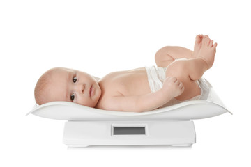 Cute little baby lying on scales against white background