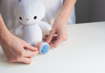 Kids medicine concept. Cute and friendly poster representing children healthcare. Nurse apply medical plaster on a leg of toy bunny.