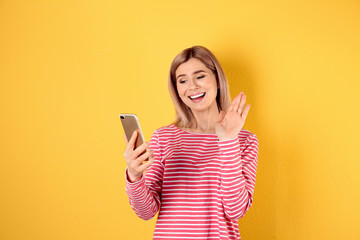 Naklejka premium Woman using mobile phone for video chat on color background