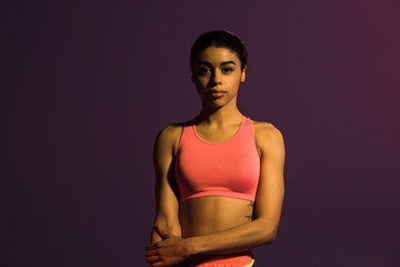Obraz premium beautiful sportive african american girl in pink sports bra looking at camera isolated on purple