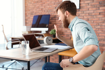 Young man using video chat on laptop in home office. Space for text