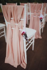 Beautiful setting for outdoors wedding ceremony. Chairs for guests of the bride and groom are decorated in the same style, decorated with fashionable fabric.  chairs are placed convolution with  rose 