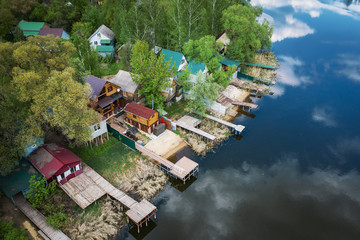 Aerial view of buildings or houses with piers on river bank among green forest and trees in summer day, beautiful rural tranquil landscape