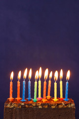 Happy Birthday Brownie Cake with Peanuts, Salted Caramel and Colorful Burning Candles on the Violet Background. Copy Space for Text.