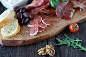 Prosciutto, bread, olives, walnut, salami, basil and cherry tomatoes on  brown wooden board.  Mediterranean kitchen.
