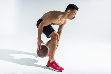 handsome mixed race man in red sneakers playing ball on white background