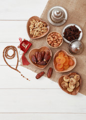 Ramadan iftar party concept. Islamic holy book Quran and rosary beads with delicious dates, dried figs, dried apricots, walnuts, almonds, raisins on bamboo plates on a white wooden table background.