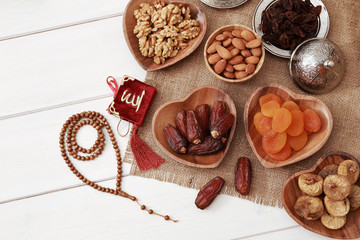 Ramadan iftar party concept. Islamic holy book Quran and rosary beads with delicious dates, dried figs, dried apricots, walnuts, almonds, raisins on bamboo plates on a white wooden table background.