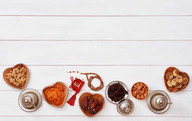 Ramadan iftar party concept. Islamic holy book Quran and rosary beads with delicious dates, dried figs, dried apricots, walnuts, almonds, raisins on bamboo plates on a white wooden table background.